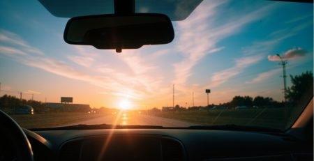 Interior view of a car windshield with a blurred, vibrant Houston skyline at sunrise. The glass shows a subtle film, highlighting the importance of windshield cleaning for clear visibility.