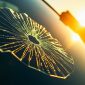 Close-up of a small, sharp windshield chip on a vehicle in Houston, illuminated by bright sunlight. The image details the cracked glass texture and subtle city skyline reflections, emphasizing the need for windshield chip repair and auto glass insurance coverage.